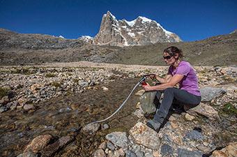 Using a pump water filter at a stream in the mountains
